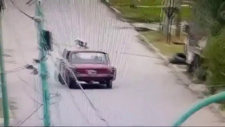 Un auto bordó circula por una calle asfaltada en subida, capturado por una cámara de seguridad.