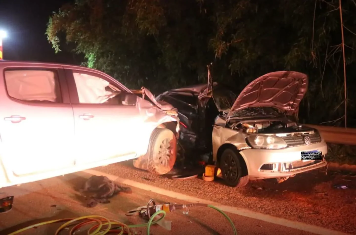 Dos autos chocados de frente sobre una ruta de noche con herramientas de rescate en el suelo.