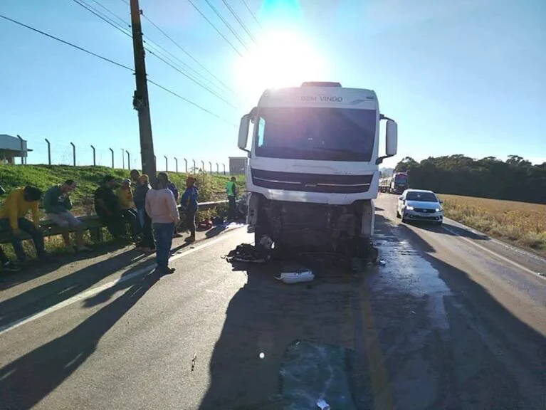 Un camión blanco chocado de frente detenido sobre una ruta con personas mirando al costado.