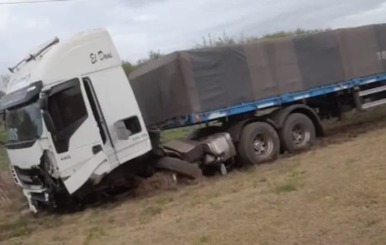 Un camión blanco con acoplado quedó varado e inclinado sobre el pasto al costado del camino.