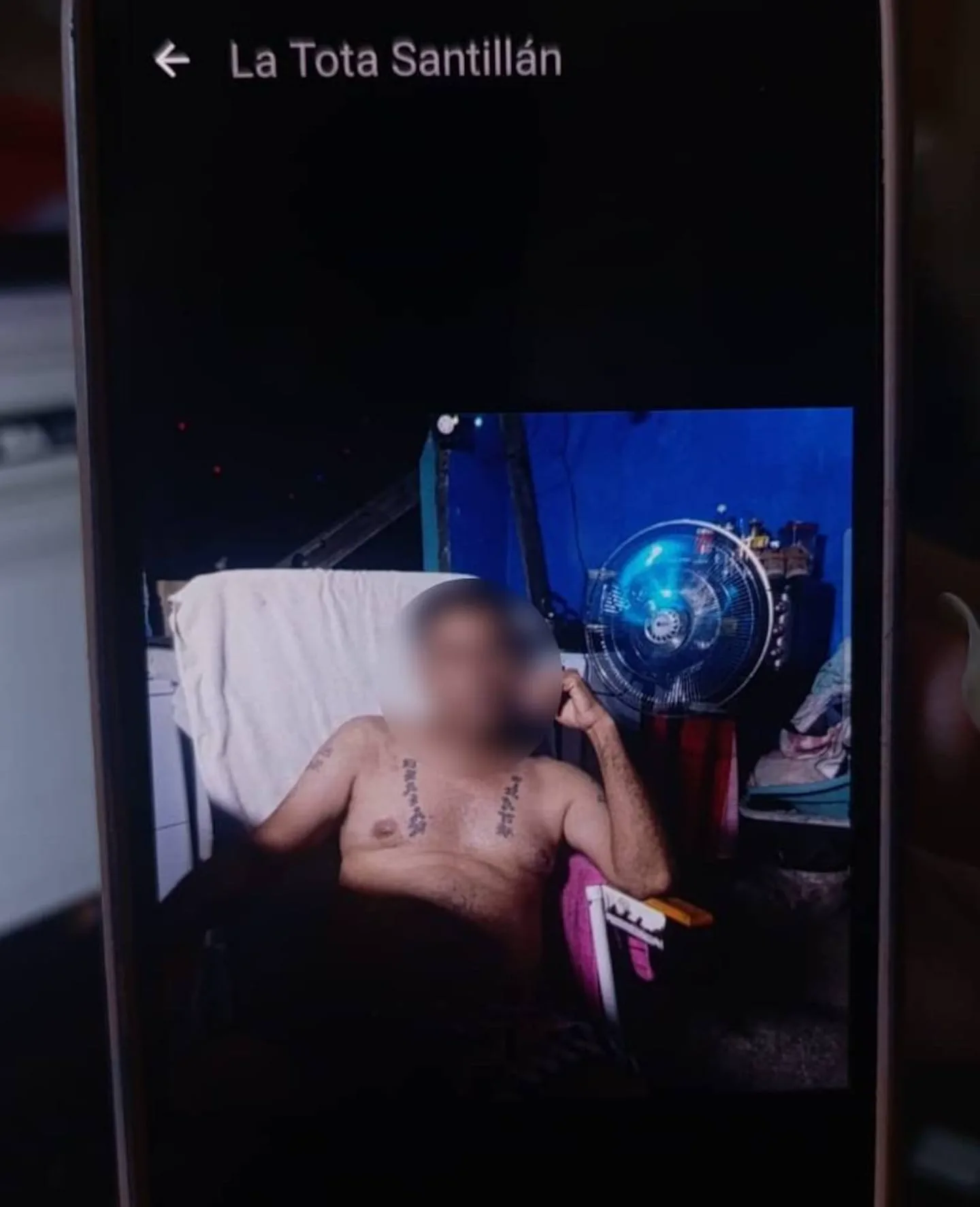 Una persona con el torso desnudo y tatuajes sentada en una silla, mostrada en la pantalla de un celular.