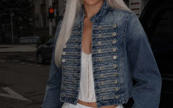 Una persona de pelo platinado viste una campera de jean con botones y una prenda blanca.
