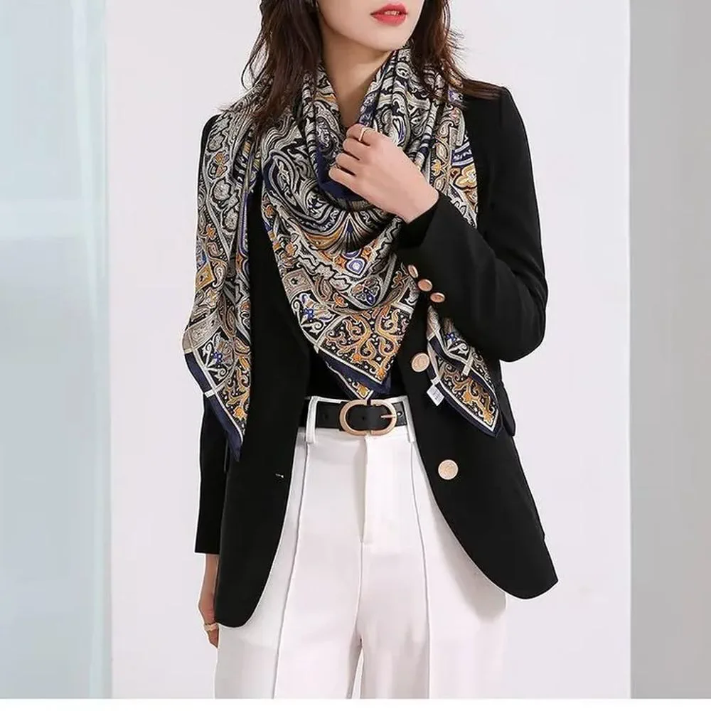 Una mujer con saco negro y pantalon blanco luce un panuelo estampado de varios colores alrededor del cuello.