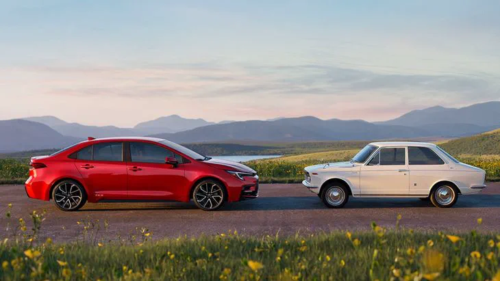 Un auto rojo moderno y un auto blanco antiguo estan enfrentados sobre un camino asfaltado con colinas de fondo.