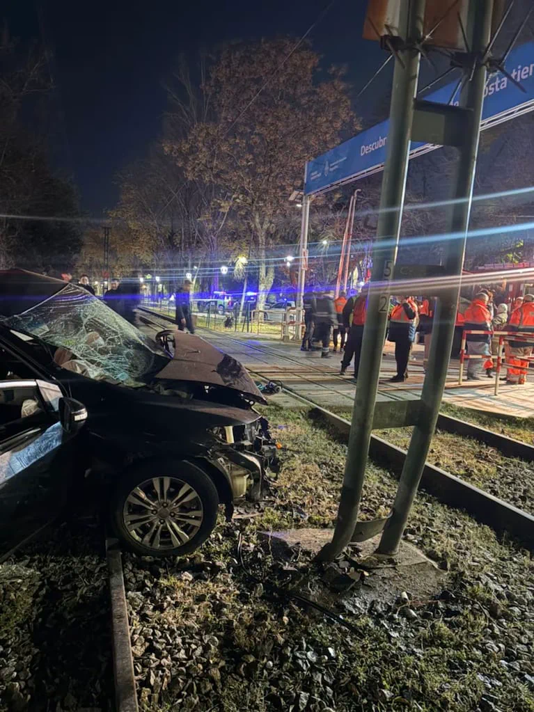 Un auto negro chocado contra un poste ferroviario queda sobre las vías cerca de un paso a nivel.