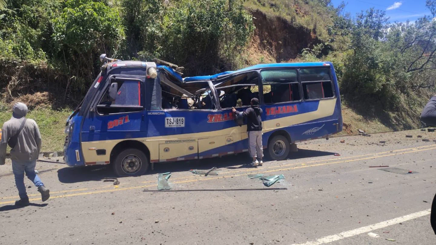 Un colectivo azul y crema con daños graves en el techo y ventanas está detenido al costado de una ruta.