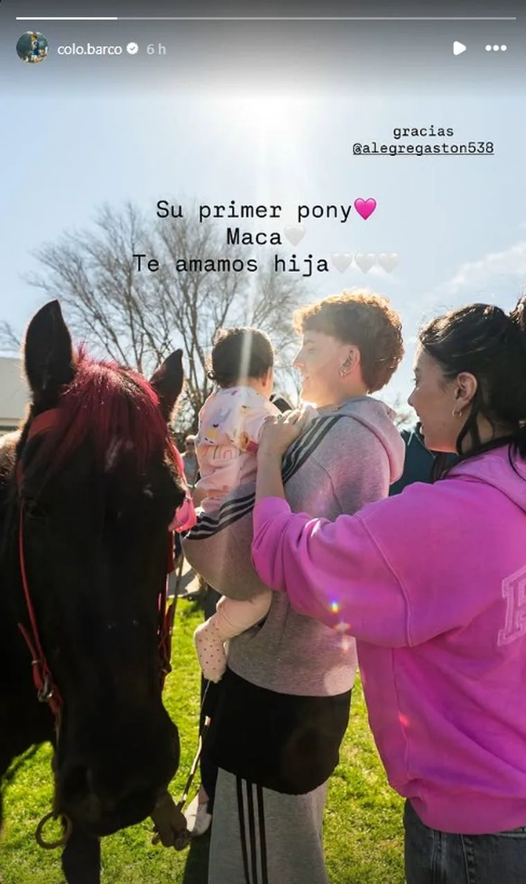 El futbolista Valentín Barco y Yazmín Jaureguy sostienen a una beba junto a un pony negro al aire libre.