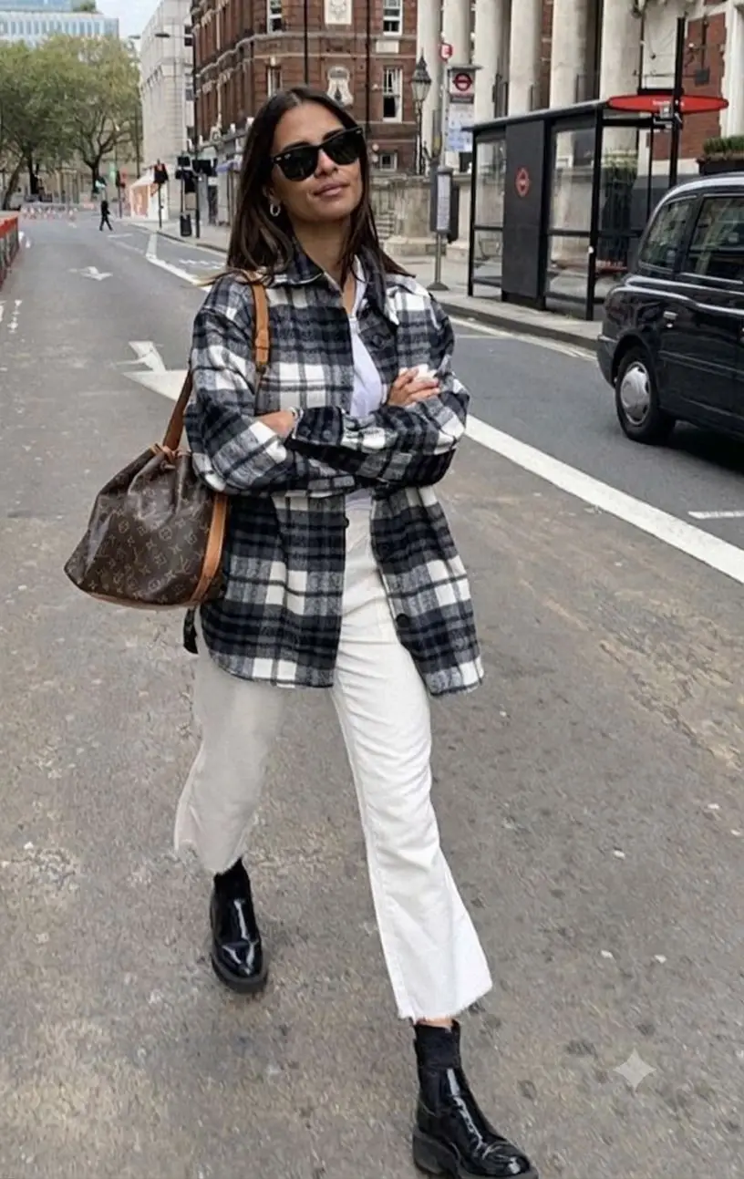 Una mujer con anteojos oscuros, camisa a cuadros y pantalon blanco camina con los brazos cruzados por la calle.
