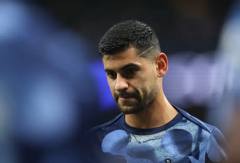 Cristian Cuti Romero mira hacia abajo con expresión seria vistiendo una camiseta azul oscura.