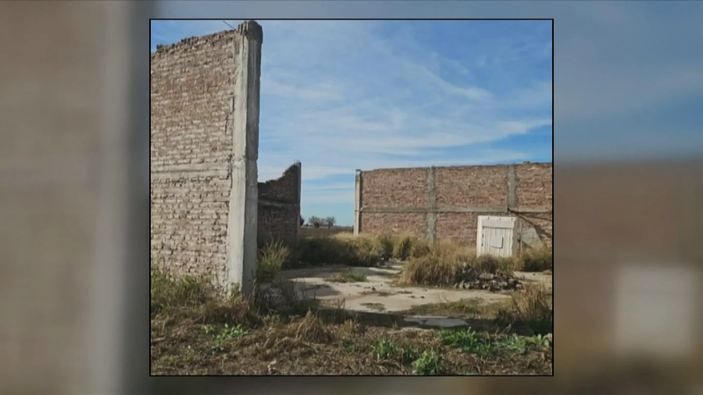 Paredes de ladrillo visto sin techar en un terreno descampado con malezas secas bajo el cielo despejado.
