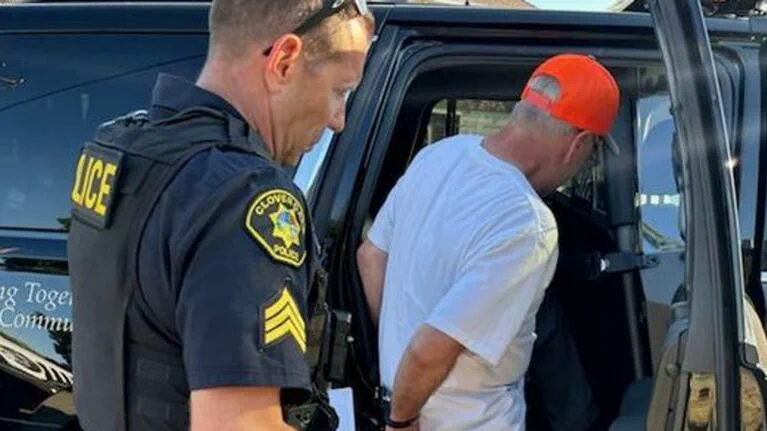 Un policía sostiene a un hombre esposado que está por subir a una camioneta.