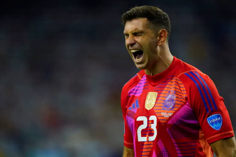 El arquero Emiliano Martínez grita con la boca abierta vistiendo la camiseta roja número 23 de Argentina.