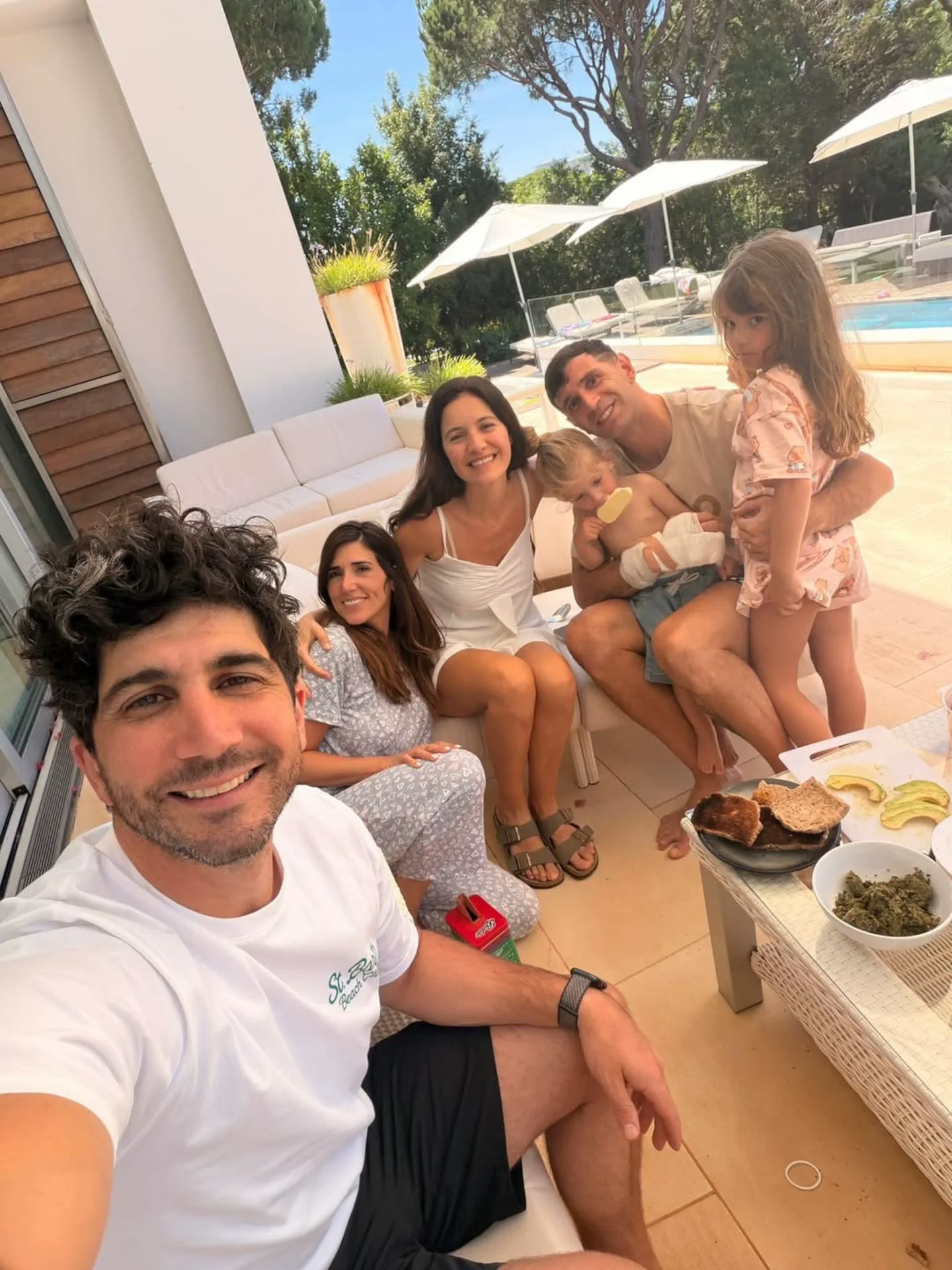 Emiliano Martinez posa en una terraza junto a su familia y un grupo de personas sentadas al sol.