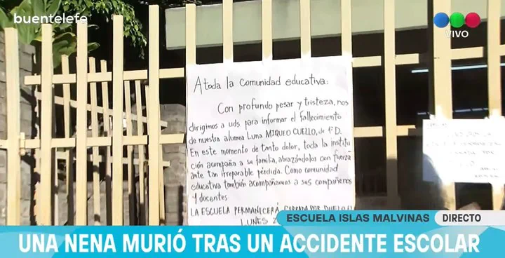 Un cartel pegado a una reja metálica blanca con un comunicado manuscrito frente a una escuela.