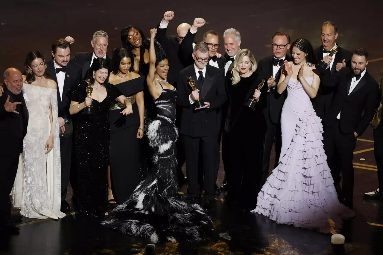 Un elenco de actores y productores en vestimenta de gala festeja sobre un escenario sosteniendo estatuillas de los Oscar.