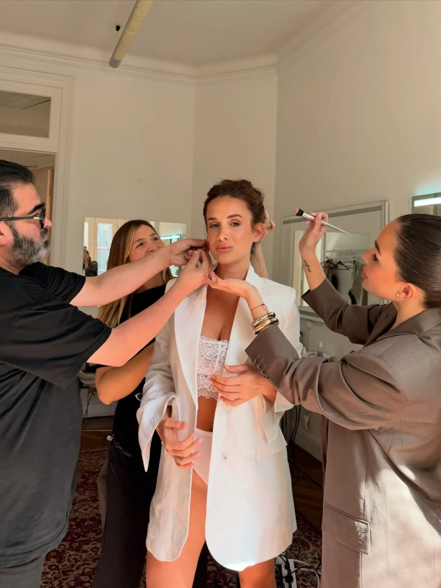 Camila Homs con saco blanco y ropa interior de encaje atendida por un equipo de estilismo.