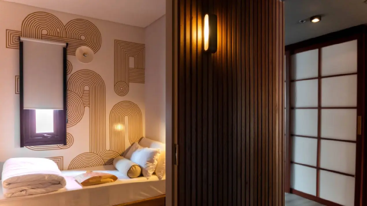 Un dormitorio con cama armada, pared decorada con líneas curvas y un panel divisor de madera.