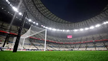 Un arco de fútbol sobre el césped de una cancha dentro de un estadio techado e iluminado.