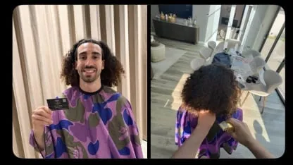 Un hombre con capa de peluquería sostiene una tarjeta y en otra toma le cortan el pelo con una máquina.