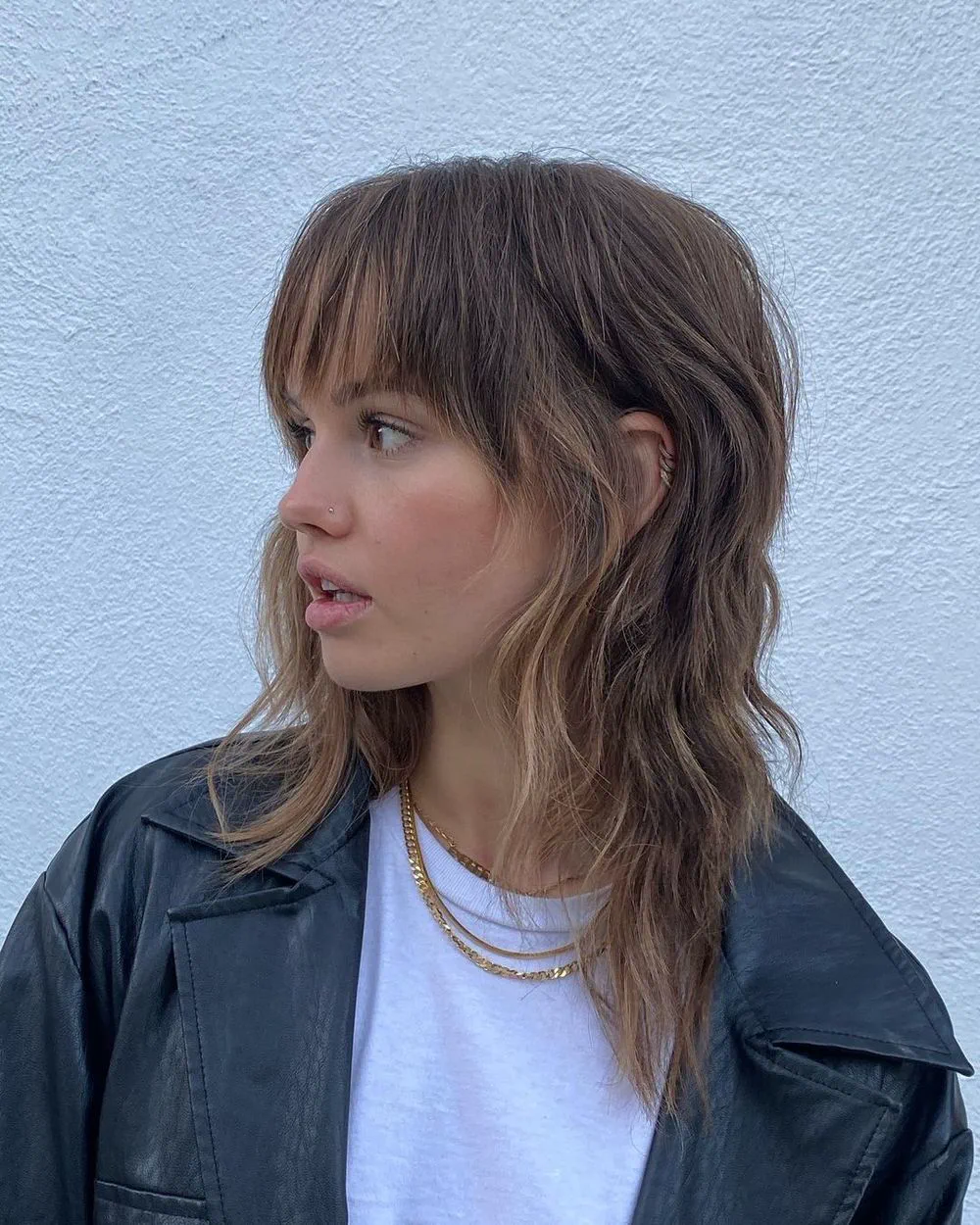 Una mujer de perfil con corte shaggy y flequillo viste remera blanca y campera de cuero.