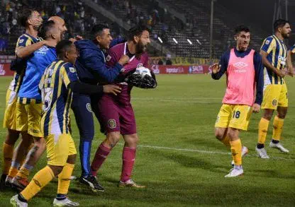 Futbolistas de Rosario Central festejan efusivamente con su arquero en el campo de juego.