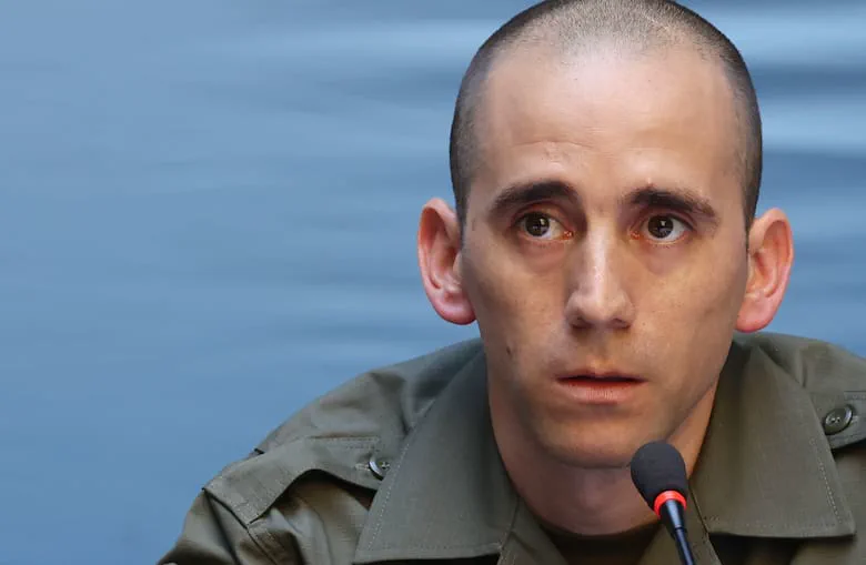 Un hombre rapado con uniforme militar verde habla frente a un micrófono.