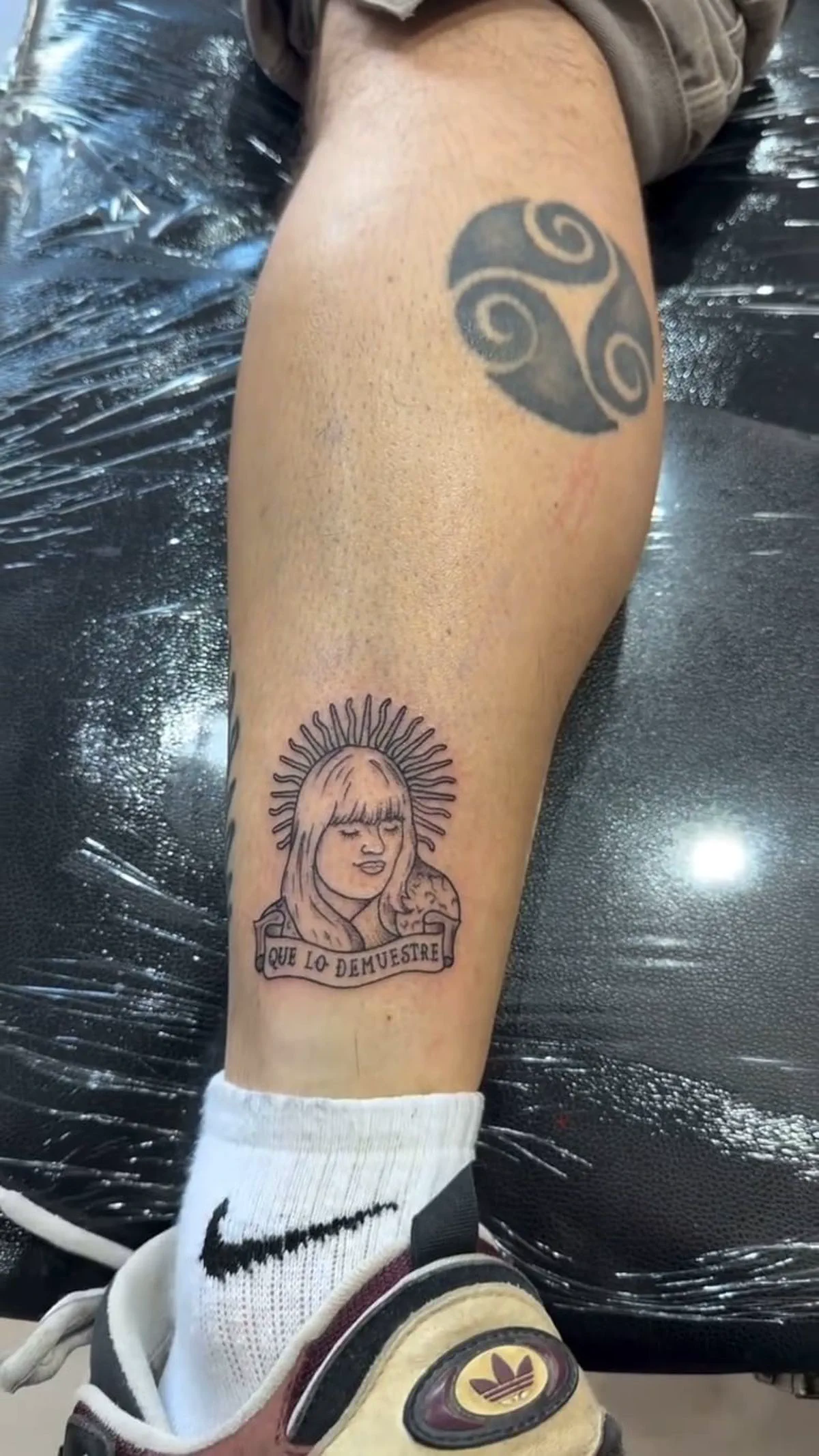 Un tatuaje en la pierna muestra el rostro de una mujer con rayos de sol y la frase Que lo demuestre.