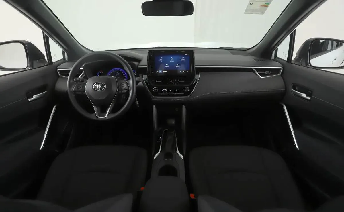 El habitáculo delantero de un auto con volante multifunción, pantalla táctil y asientos oscuros.