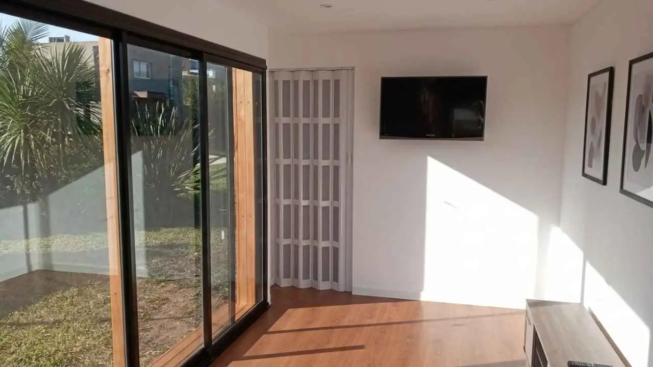 Una habitacion con piso flotante, un ventanal corredizo que da al patio, un televisor en la pared y una puerta plegadiza.