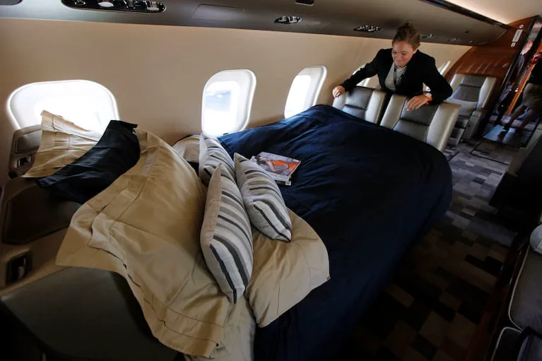 Una azafata acomoda los almohadones sobre una cama armada adentro de un avión privado.