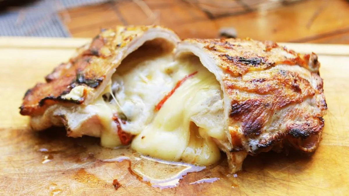 Un trozo de carne relleno con queso fundido cortado a la mitad sobre una tabla de madera.