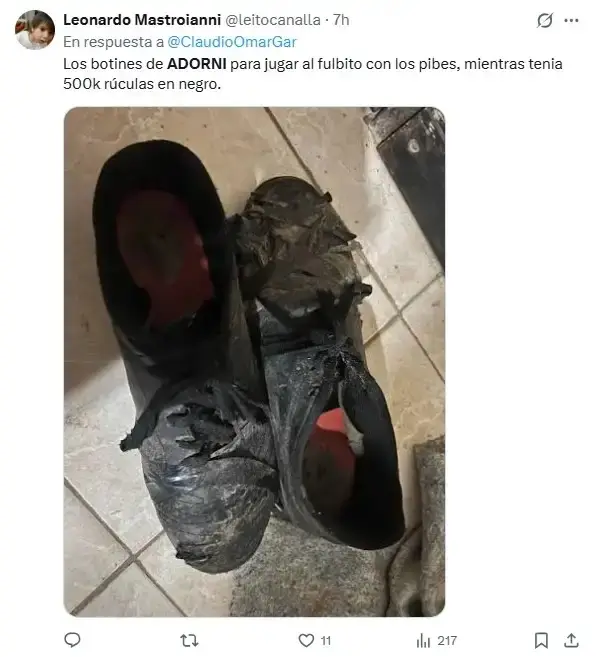 Captura de un tuit que muestra un par de botines negros rotos y gastados sobre un piso de baldosas.