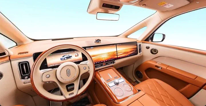 El tablero y volante de tono claro y marron en el habitaculo delantero de un auto moderno con amplias pantallas.
