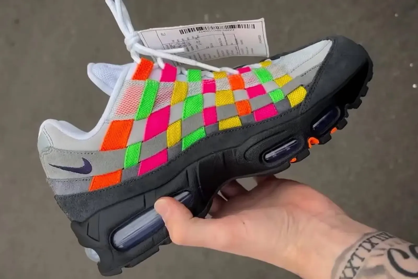 Una mano sostiene una zapatilla Nike con un diseño entretejido de tiras multicolor y suela negra.