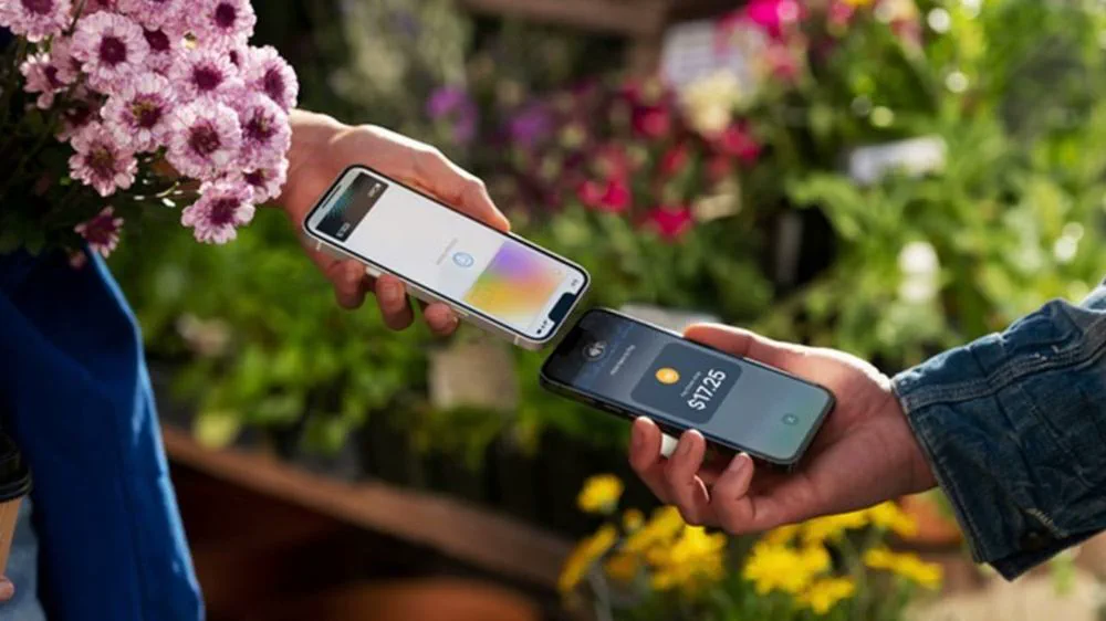 Dos personas acercan sus teléfonos celulares para realizar un pago sin contacto en un puesto de flores.