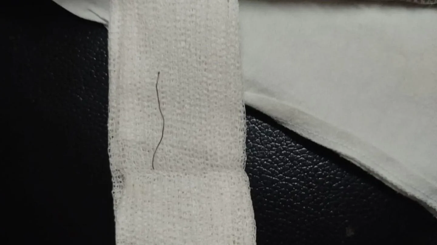 Un pelo fino y ondulado descansa sobre una tira de gasa blanca apoyada en una superficie oscura.