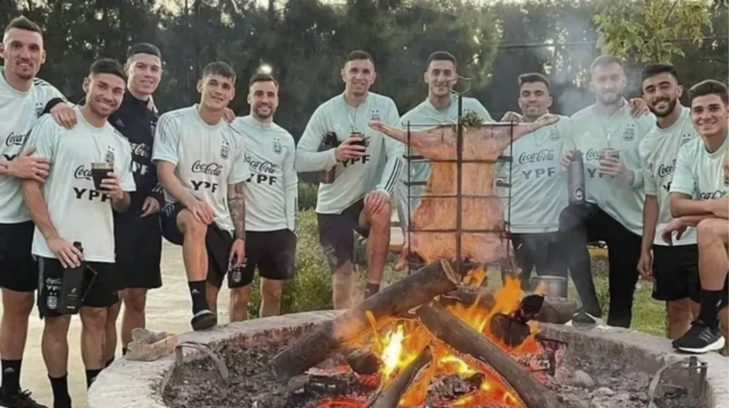 Futbolistas de la Selección Argentina posan de noche alrededor de un fogón con un cordero a la estaca.