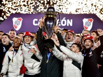 Jugadores del plantel de River Plate levantan un trofeo en un festejo nocturno con fuegos artificiales.