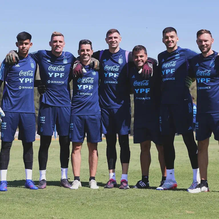 Futbolistas y cuerpo técnico de la selección argentina posando abrazados en una cancha de entrenamiento.