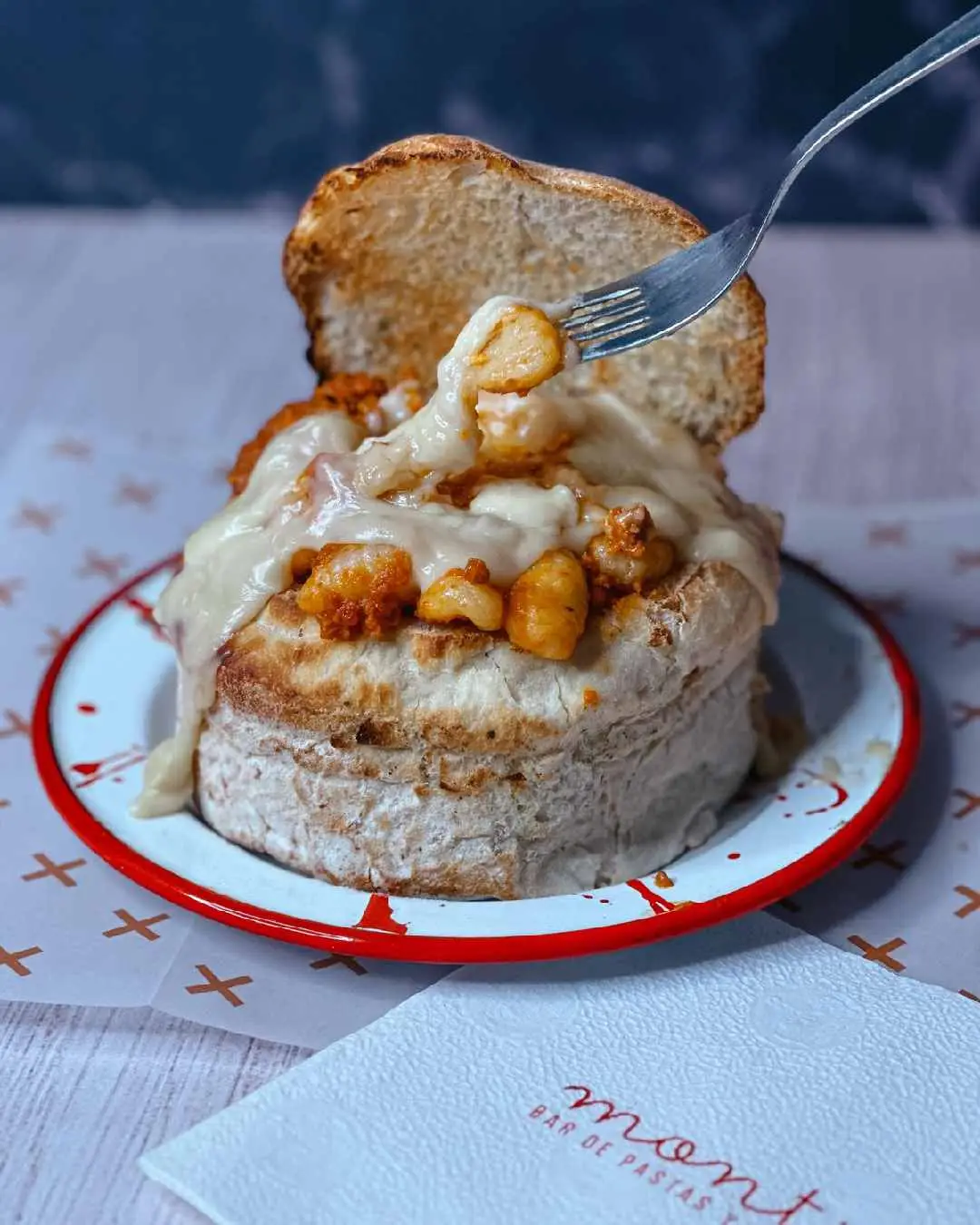 Un pan relleno de ñoquis con salsa y queso derretido pinchado por un tenedor en un plato.