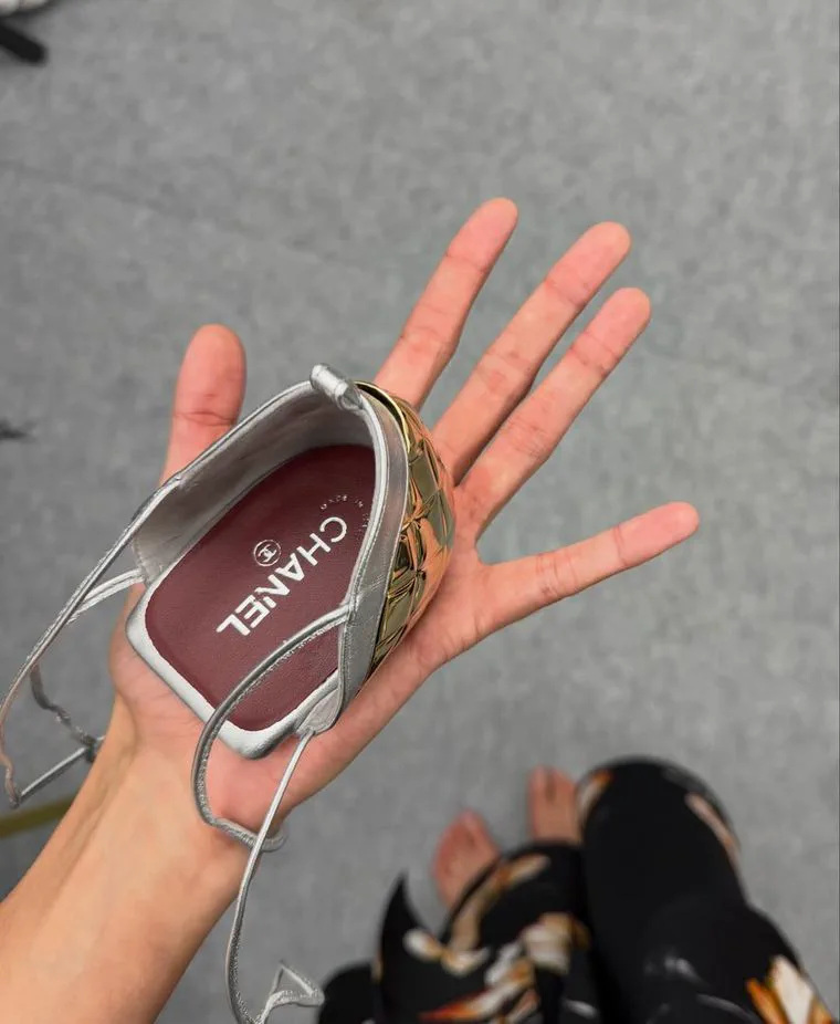 Una mano sostiene la parte trasera de un zapato plateado de taco dorado de marca Chanel.