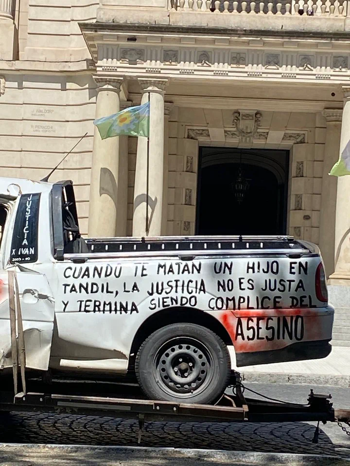 La caja de una camioneta blanca con leyendas de protesta pintadas sobre un tráiler frente a un edificio.
