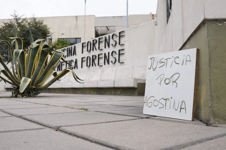 Un cartel con el texto "Justicia por Agostina" apoyado en la vereda frente a un edificio.