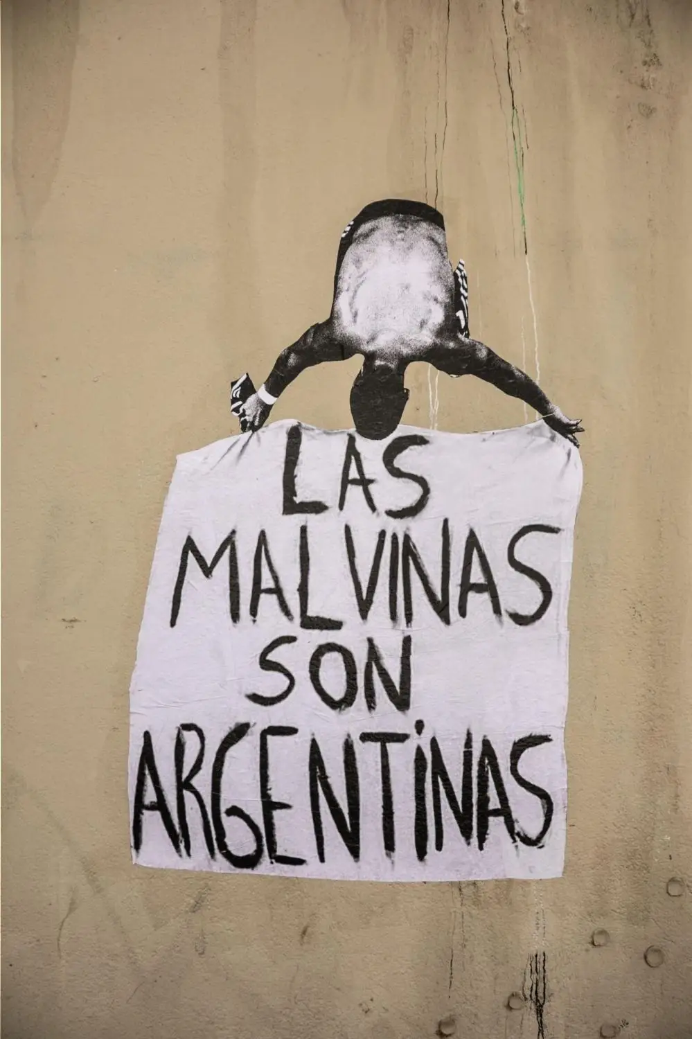 Afiche pegado en una pared que muestra a una persona de espaldas sosteniendo un cartel sobre las Islas Malvinas.