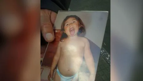 Una mano sostiene el retrato de una nena en panales sacando la lengua.