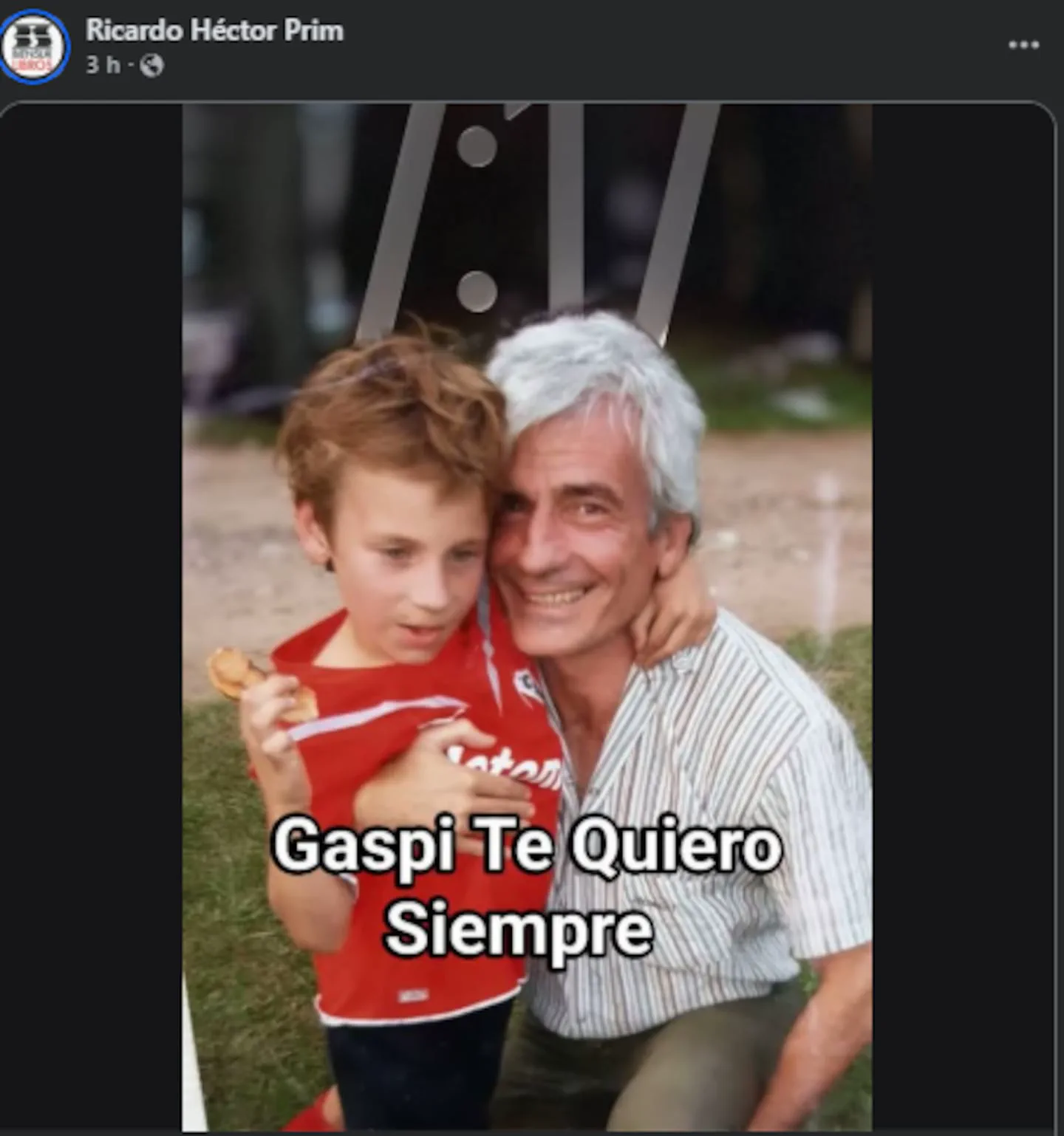 Un hombre mayor de pelo canoso sonríe abrazando a un nene con camiseta roja de fútbol al aire libre.