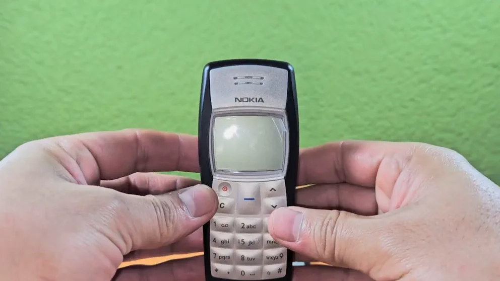 Dos manos sosteniendo de frente un teléfono celular clásico con pantalla apagada.
