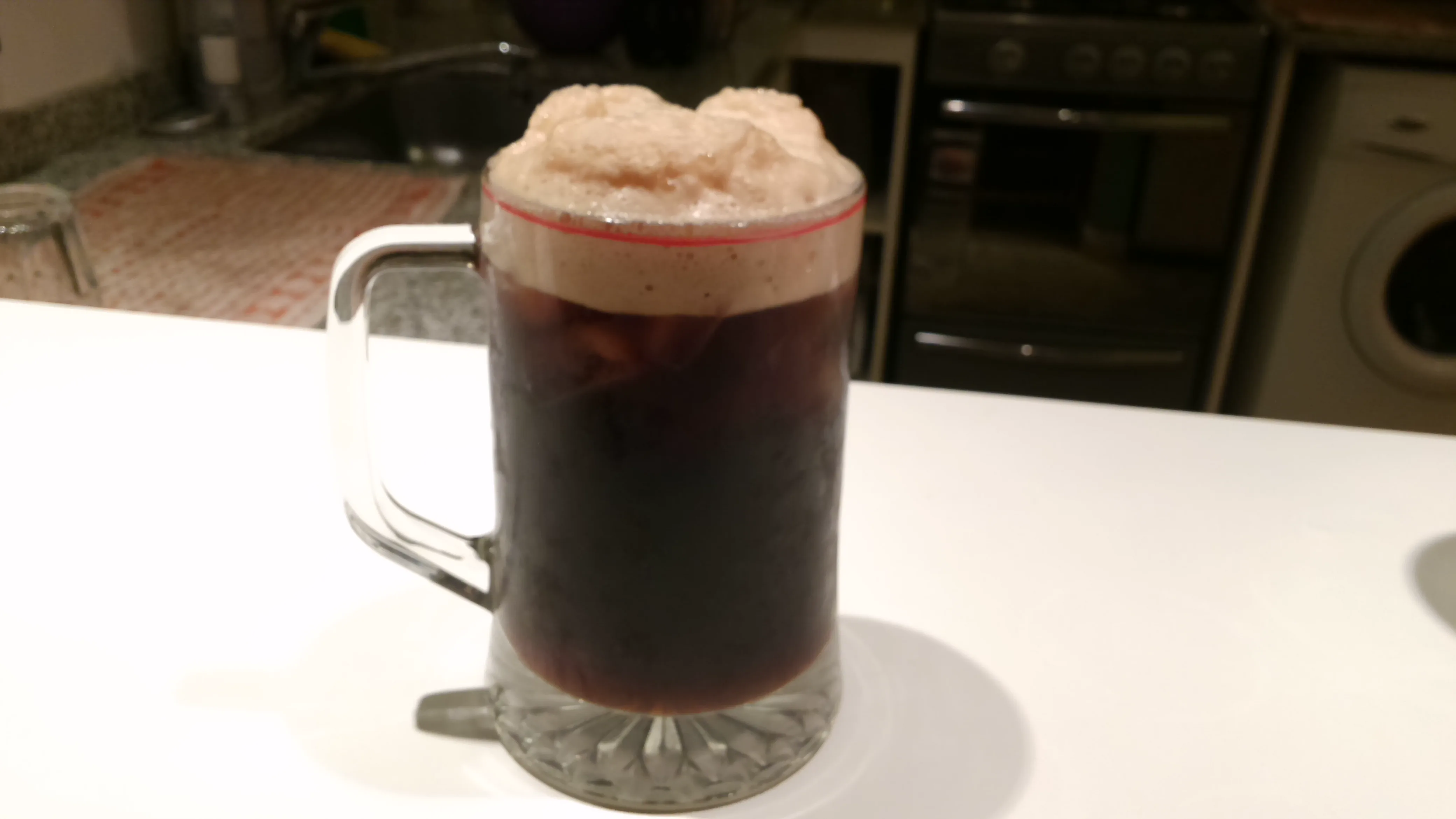 Un vaso de fernet con espuma se encuentra servido sobre una mesada blanca en una cocina.