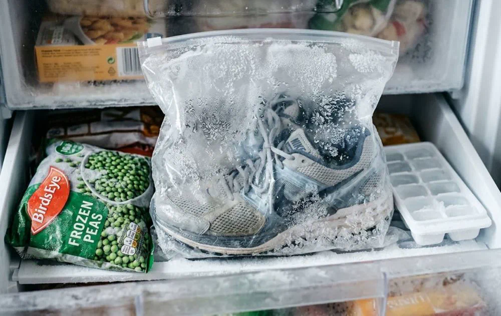 Unas zapatillas dentro de una bolsa plástica transparente con hielo reposan en un congelador junto a arvejas congeladas.