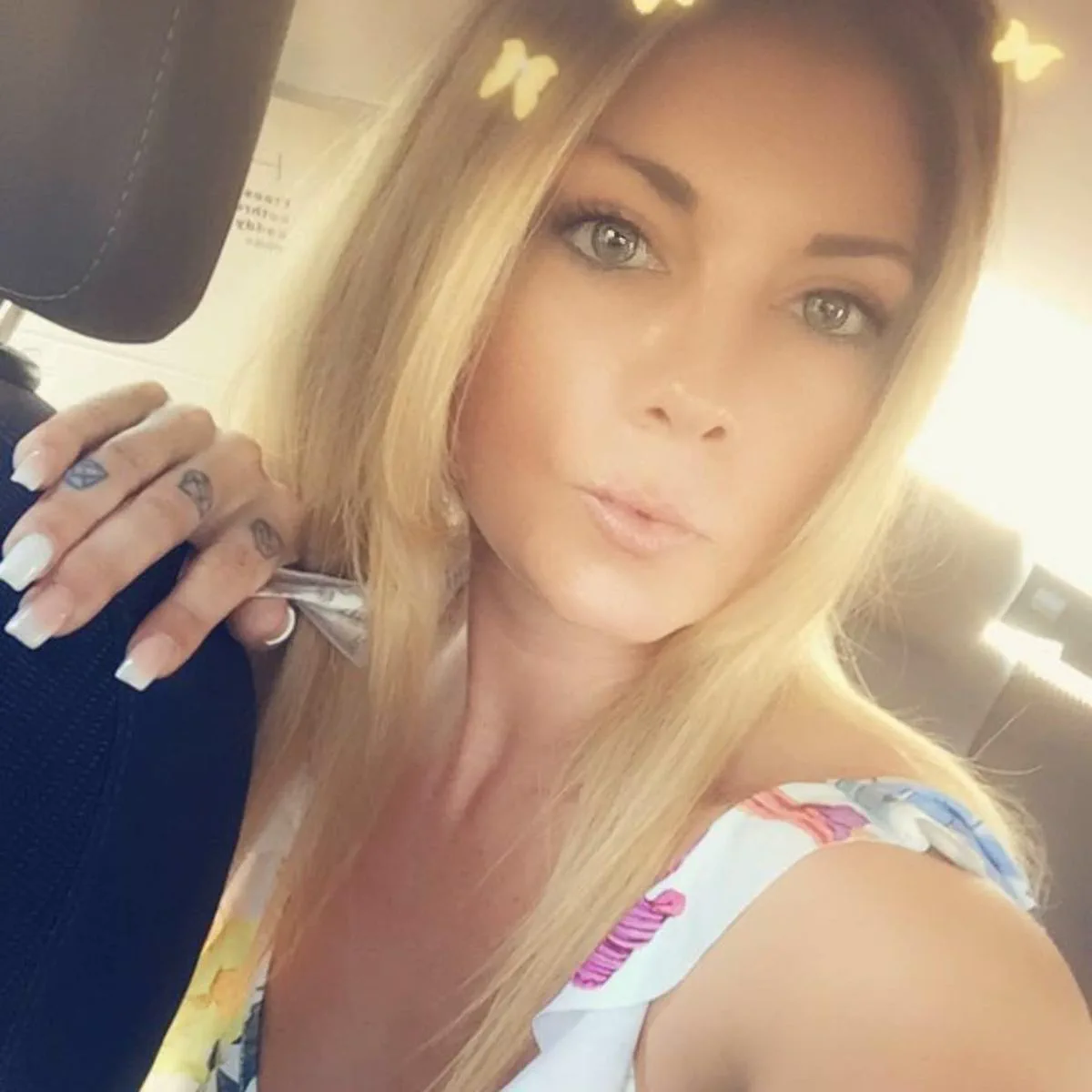 Una mujer rubia sentada dentro de un auto se saca una selfie mirando a la camara.